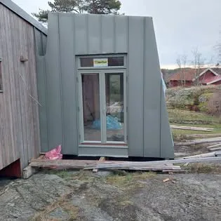 Grå-grön plåtfasad med glasat dörrparti