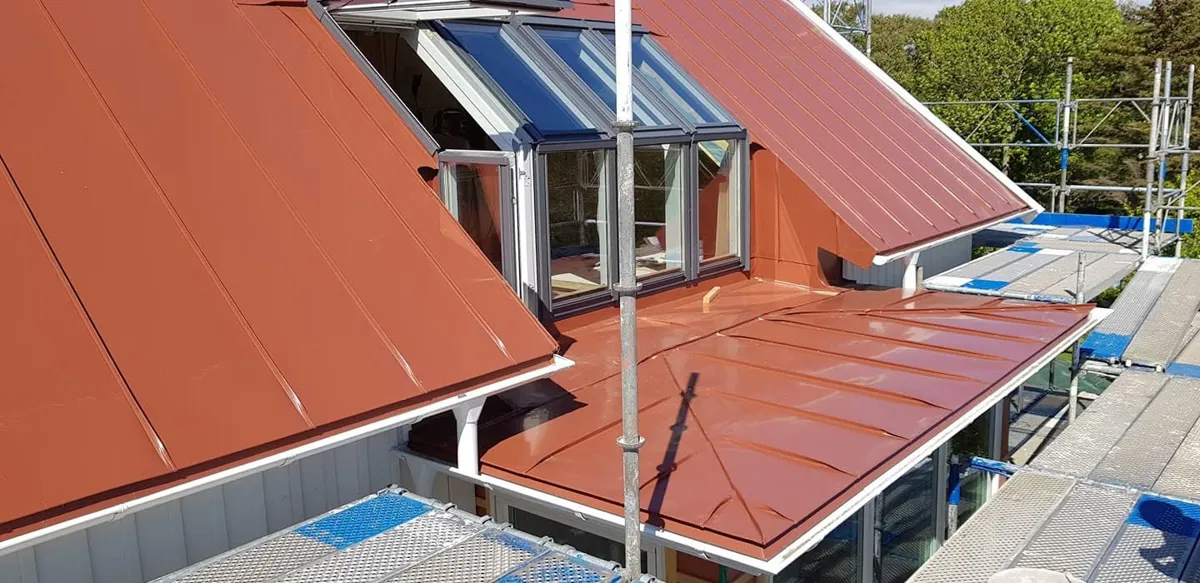 Rött bandtäckt plåttak med kupa och nya fönster, med byggställning runt huset